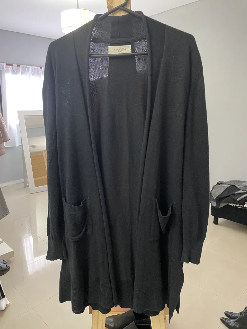 Cardigan largo de punto negro con bolsillos delanteros. Diseño liso y detalle de aplique de strass en la espalda. Ideal para un look casual y abrigado.