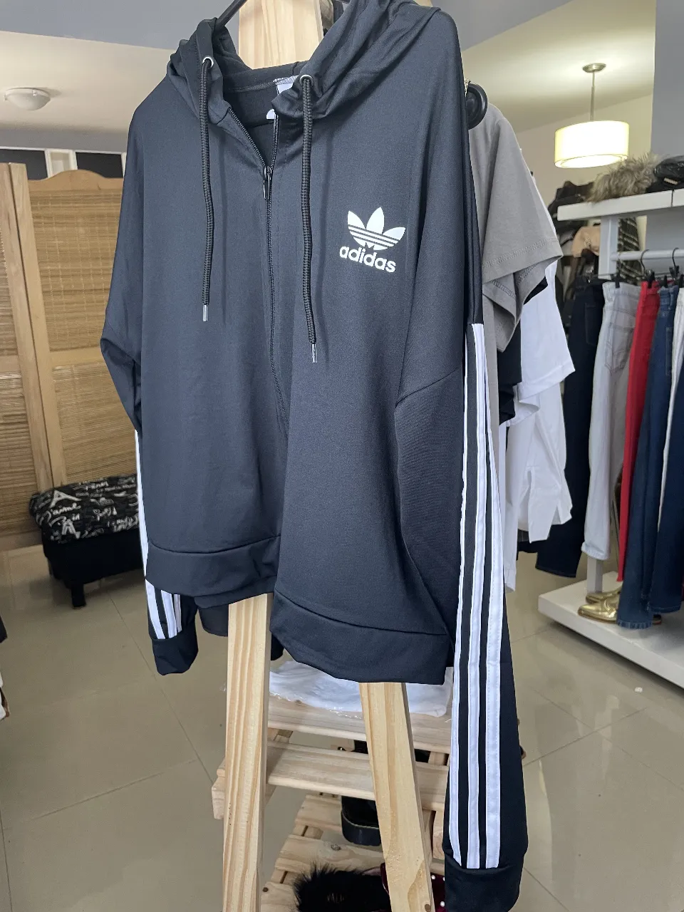 Buzo deportivo con cierre y capucha, de color negro con detalles blancos en las mangas. Ideal para un look casual y cómodo.