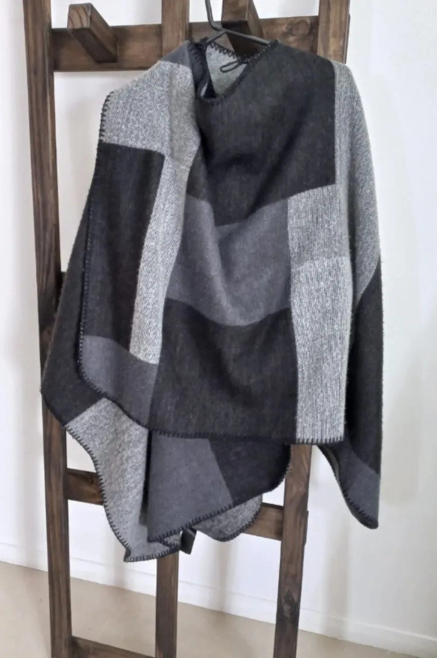 Poncho de diseño geométrico en tonos grises y negro, ideal para el invierno. Confeccionado en tejido suave y abrigado, perfecto para un look casual y cómodo.