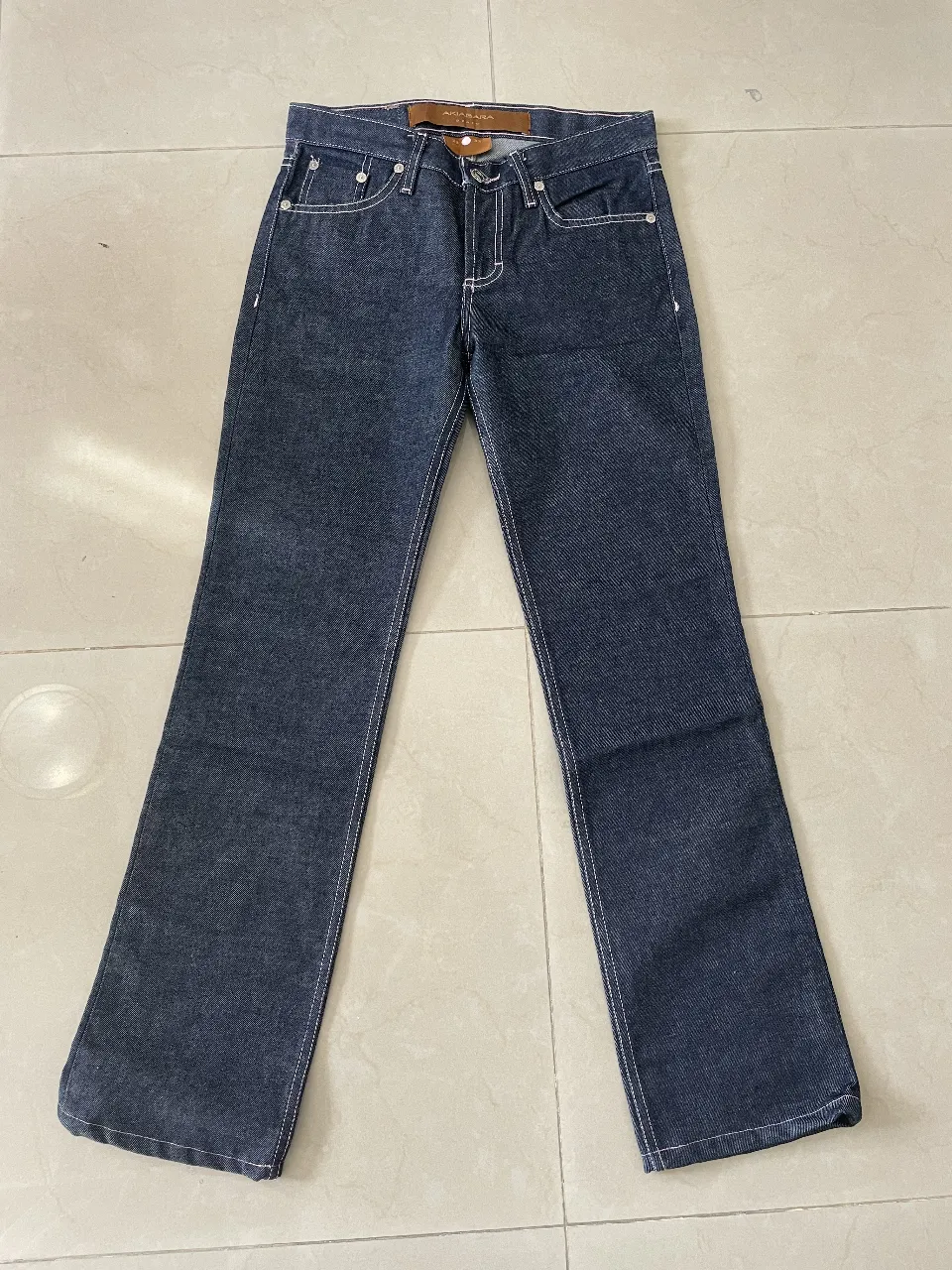 Jeans rectos de denim azul oscuro para mujer. Talle 23/32. Con detalles de costuras blancas y etiqueta de la marca Akibara Denim.
