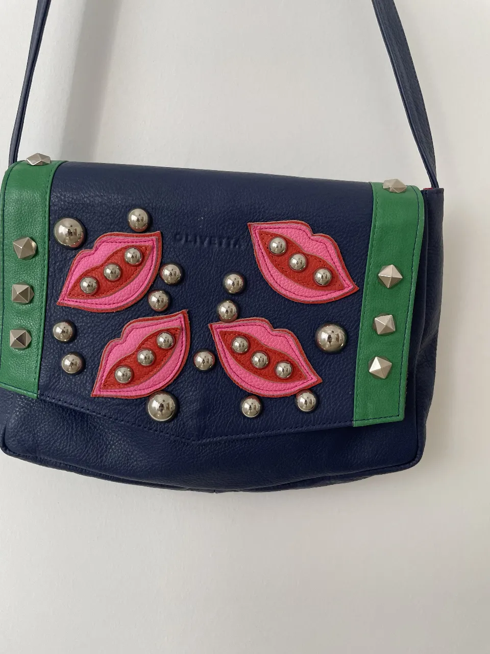 Bandolera de cuero azul marino con detalles en verde y apliques de labios rosas y plateados. Interior rosa con estampado de labios. Ideal para un look moderno y audaz.