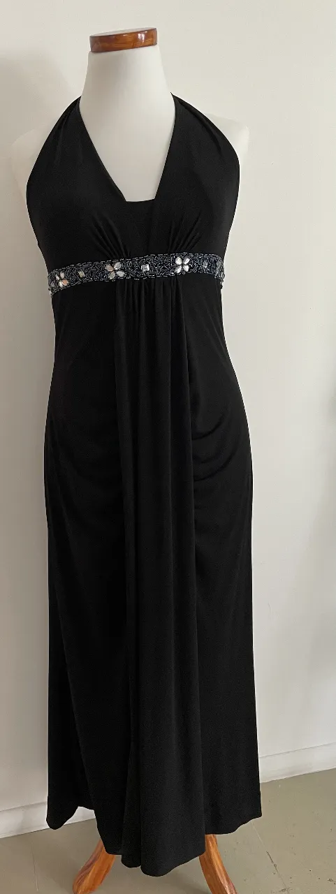 Vestido largo de fiesta negro, con escote halter y detalle de pedrería en la cintura. Ideal para eventos formales.