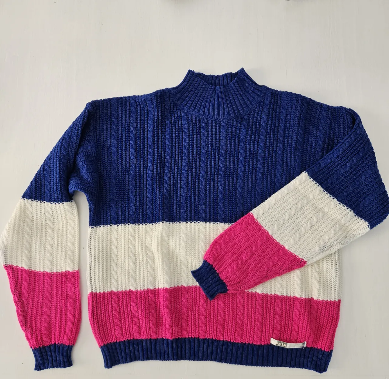 Sweater de lana tejido a rayas en azul, blanco y fucsia. Posee cuello alto y trenzas en el tejido. Ideal para un look casual y canchero.