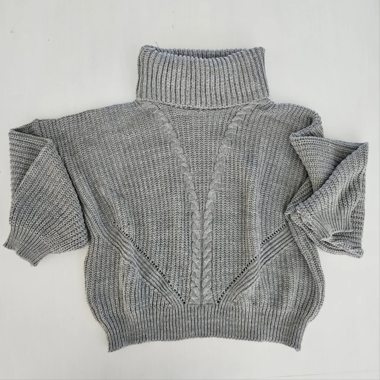 Sweater gris de lana tejido con cuello alto y detalles de trenzas en el frente. Mangas largas tipo globo y corte moderno.