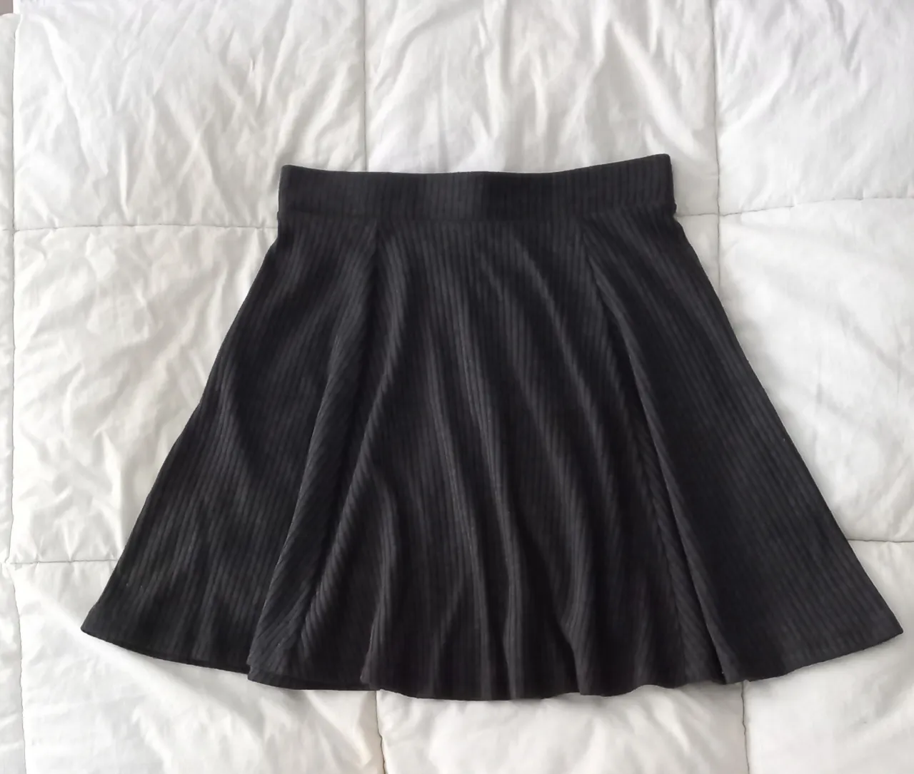 Pollera gris oscuro de lanilla gruesa acanalado, con corte evasé y cintura alta. Súper cómoda y versátil, ideal para armar looks casuales o más arreglados. Combinala con tus tops y remeras favoritas.