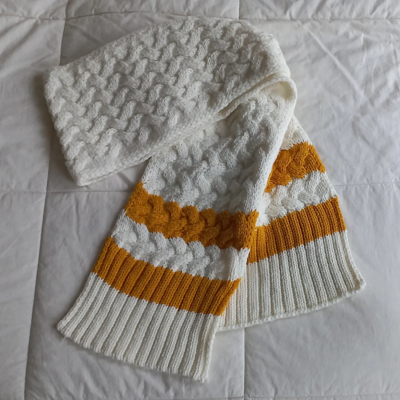 Bufanda tejida, súper abrigada y canchera. Tiene un diseño de trenzas en blanco y franjas de color mostaza
. Ideal para darle un toque de color a tus looks de invierno.