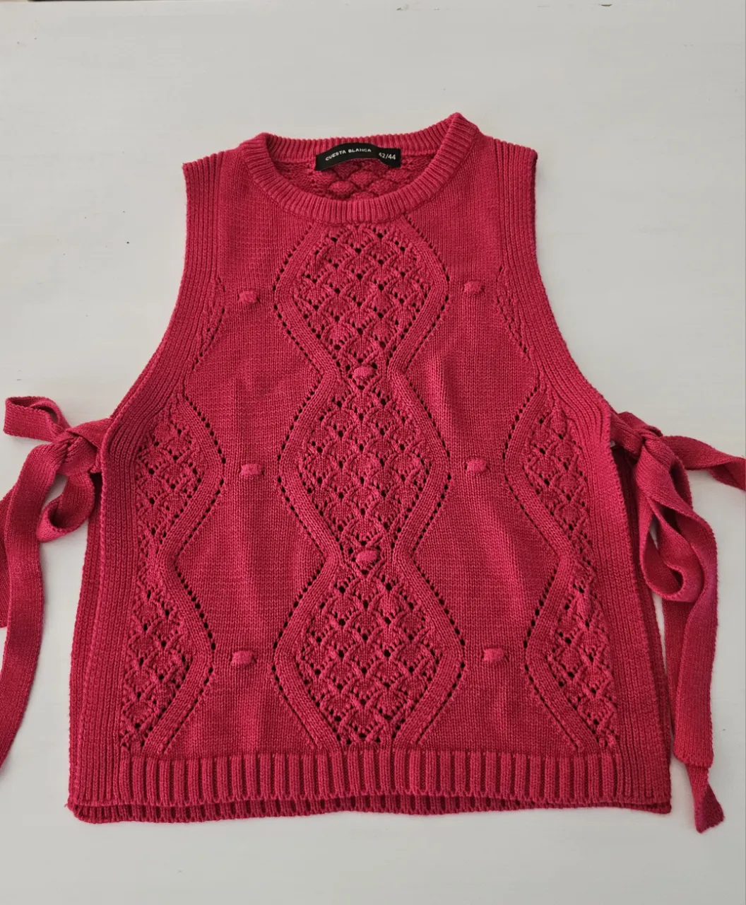 Chaleco tejido  en color fucsia vibrante, con un diseño intrincado de rombos y detalles de pompones. Posee tiras para atar en los laterales.
lo compré estando embarazada, le saque la etiqueta para lavarlo y nunca lo use. esta realmente nuevo 