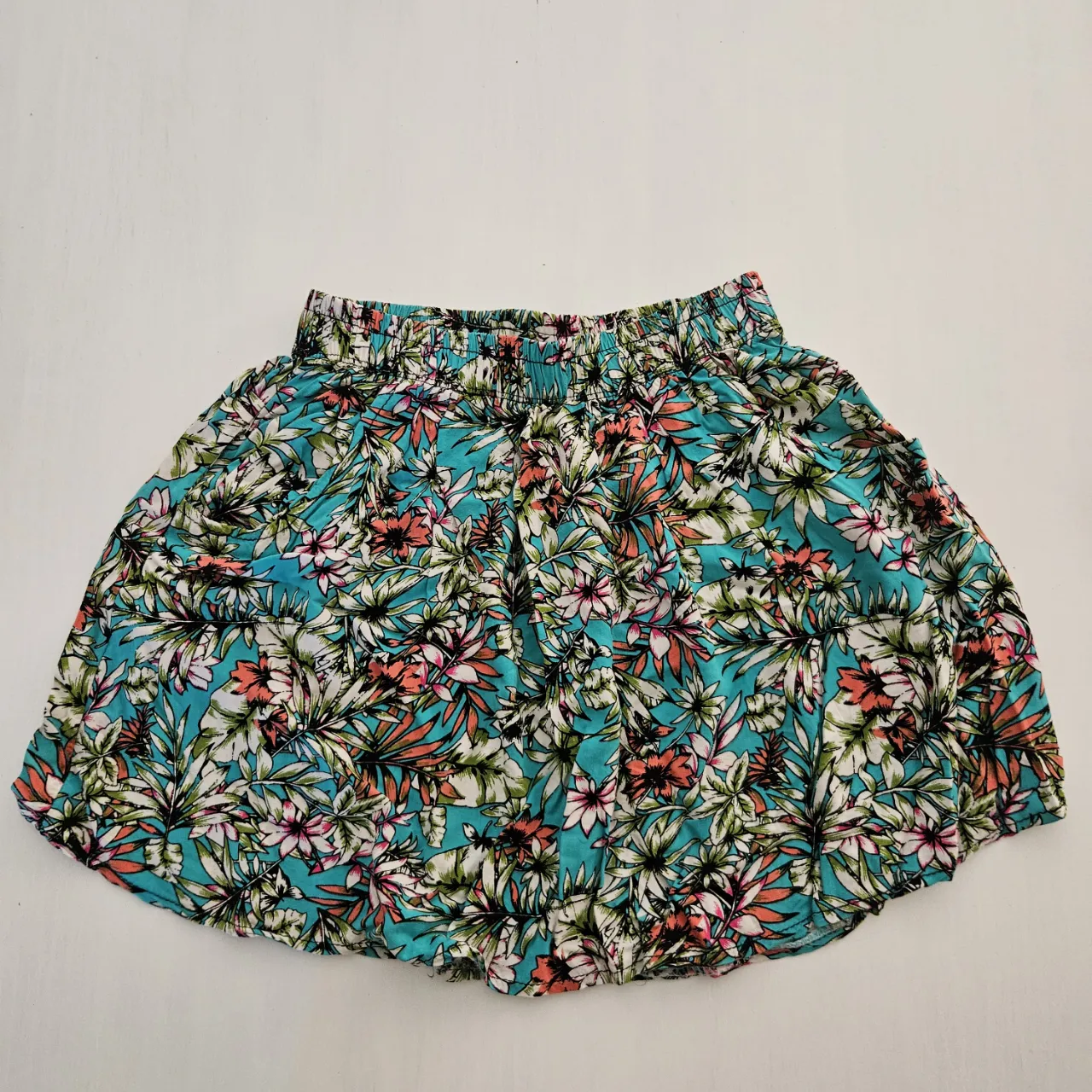 Pollera con estampado floral en tonos turquesa, blanco, rosa y negro. Cintura elastizada y bolsillos laterales.