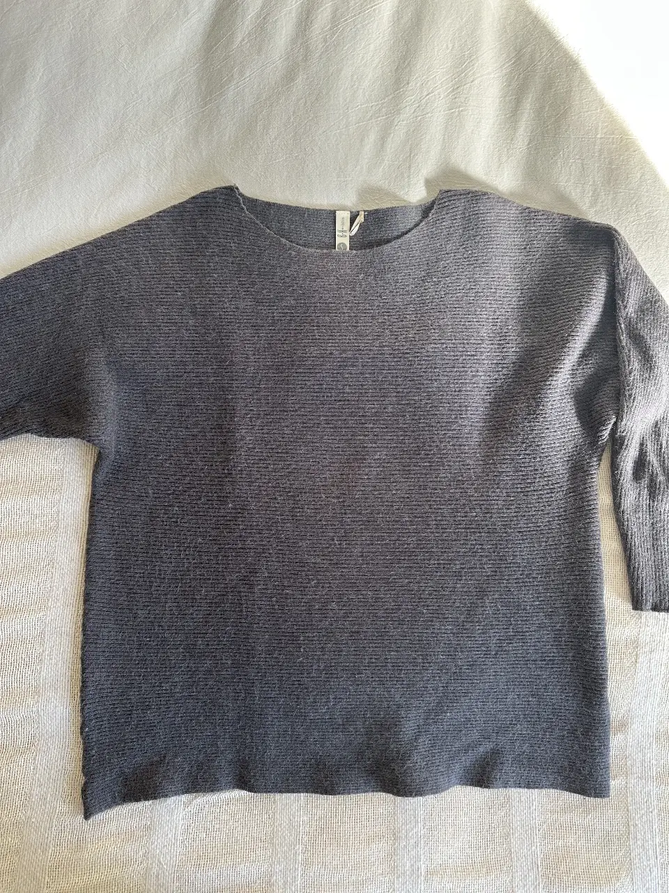 Sweater gris de tejido grueso, con mangas 3/4 y cuello redondo. Ideal para un look casual y cómodo.