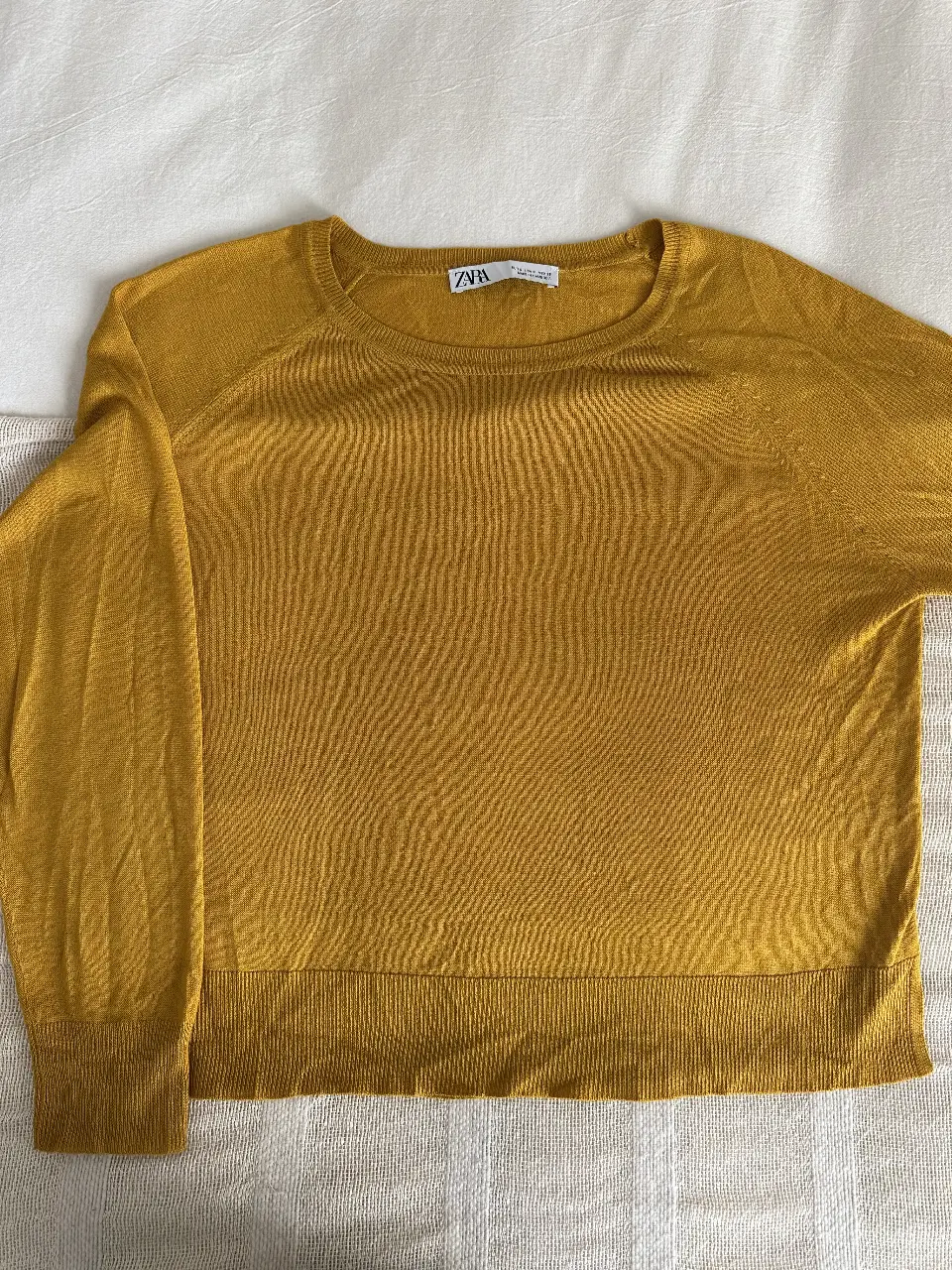 Sweater de mujer color mostaza, de la marca Zara. Confeccionado en tejido ligero y suave, ideal para media estación. Cuello redondo y mangas largas. Un básico versátil para cualquier guardarropa.