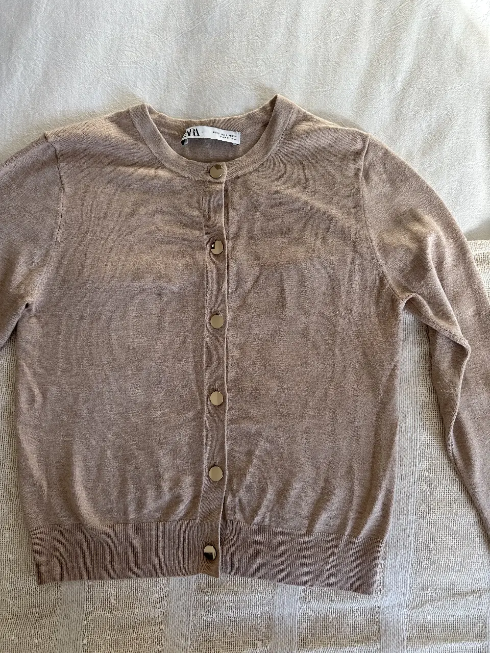 Cardigan de punto color crudo de Zara, con botones dorados. Ideal para un look casual y elegante.