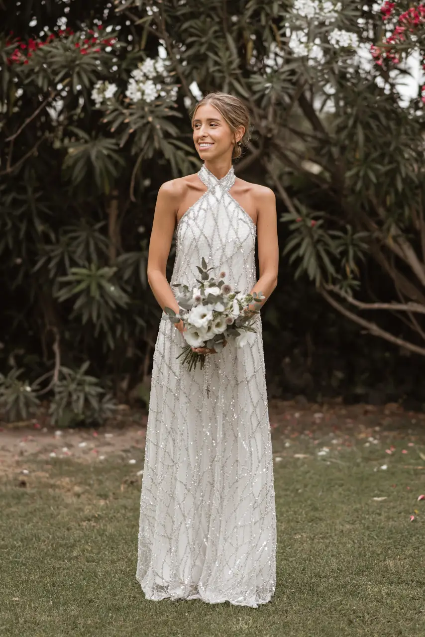 Vestido de novia largo con cuello halter y espalda descubierta. Diseño con detalles de pedrería plateada que le dan un toque elegante y sofisticado. 3 capas de telas, satén de Forreria doble, por ensima una red con hilos plateados y la tela madre es una tela bordada transparente con piedras en plata