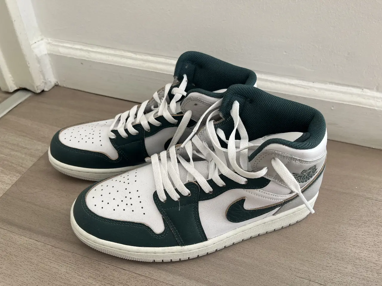 Zapatillas Air Jordan 1 Mid en cuero blanco y verde oscuro. Diseño icónico, ideales para un look urbano y deportivo.