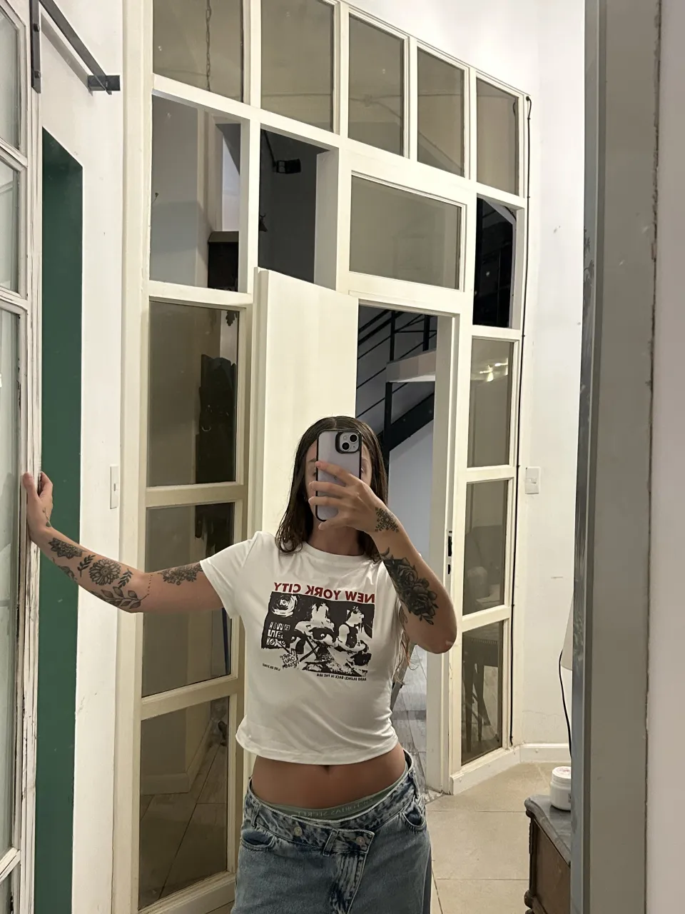 Remera blanca de manga corta con estampa "New York City" en el frente. La estampa es un collage de imágenes en blanco y negro con texto.