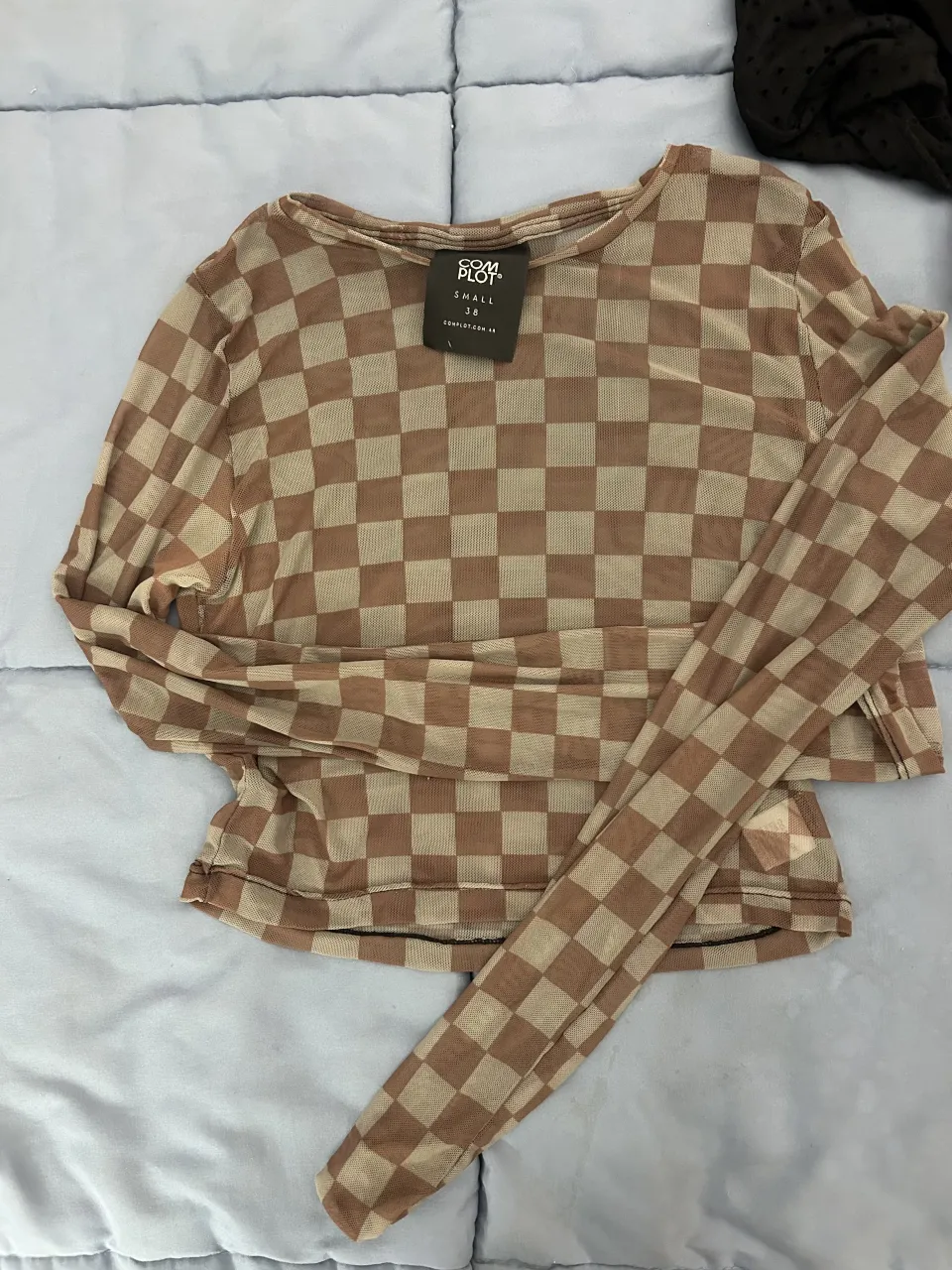 Remera manga larga de red con estampa a cuadros. Posee cuello redondo y terminación fruncida en puños y ruedo.