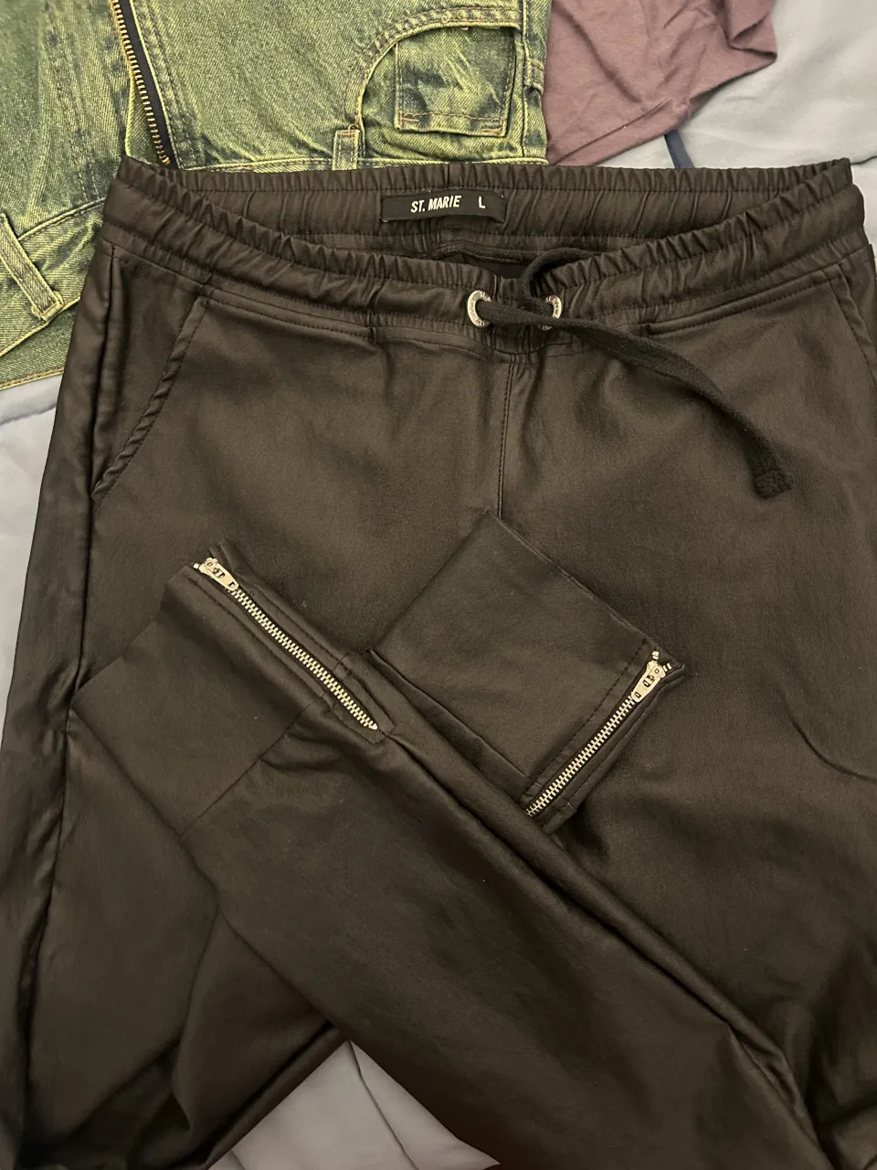 Pantalón engomado tipo babucha, negra con cordón en la cintura y cierres metálicos en los tobillos.