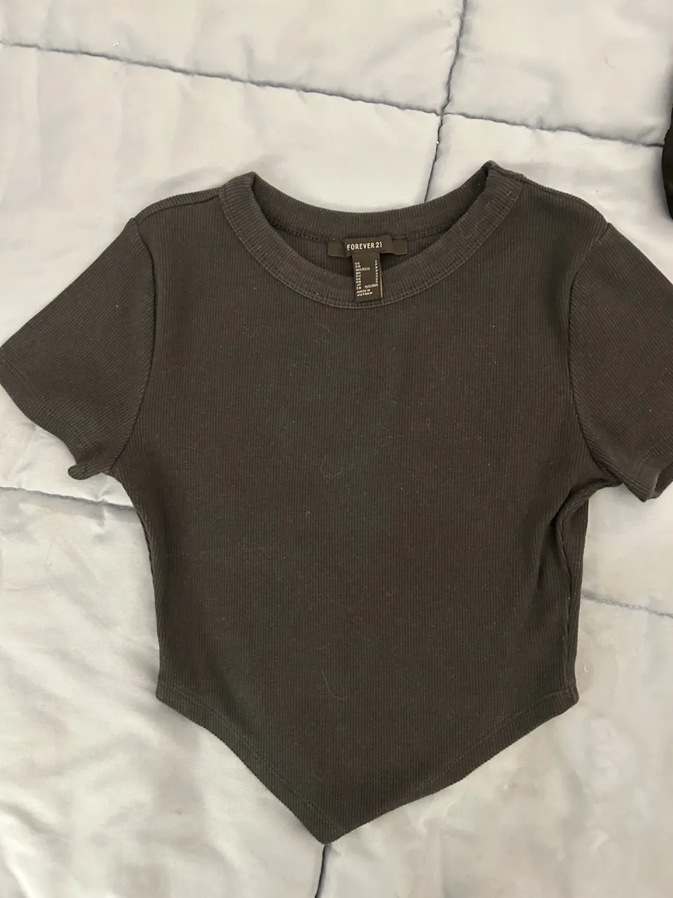 top negro de manga corta con cuello redondo y terminación en pico en la parte inferior. La tela es acanalada.