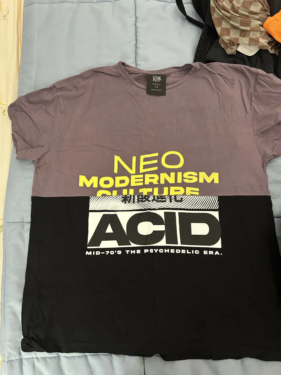 Remeron de manga corta con estampa "NEO MODERNISM CULTURE ACID MID-70'S THE PSYCHEDELIC ERA.". La parte superior es de color lila y la inferior negra.