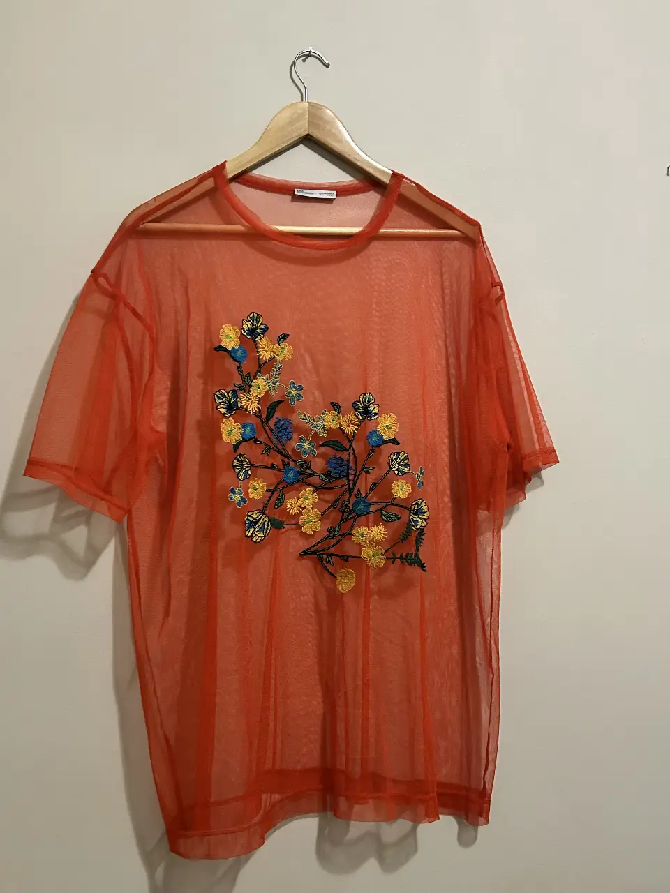 Remera de red naranja con bordado floral en tonos amarillos y azules. Ideal para un look casual y fresco.