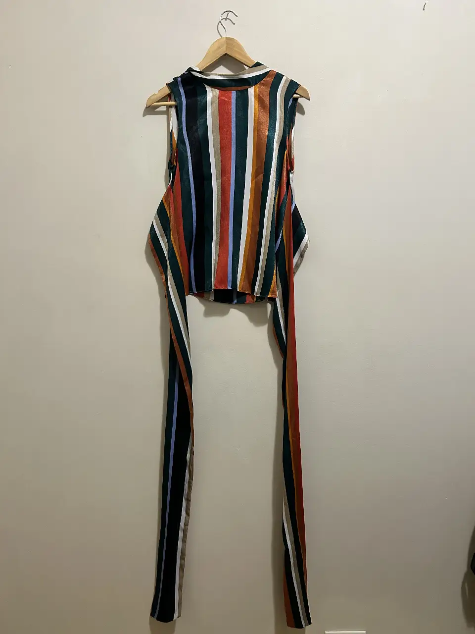 Blusa sin mangas con estampado a rayas multicolores. Tiene un cierre en el cuello y cintas largas para atar en la cintura.