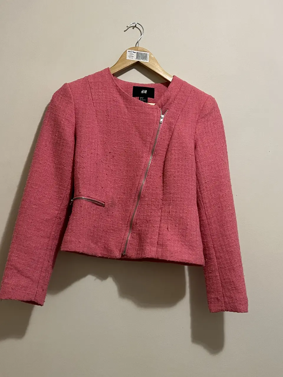 Chaqueta blazer rosa de H&M, con cierre asimétrico y textura tweed. Ideal para un look elegante y moderno.