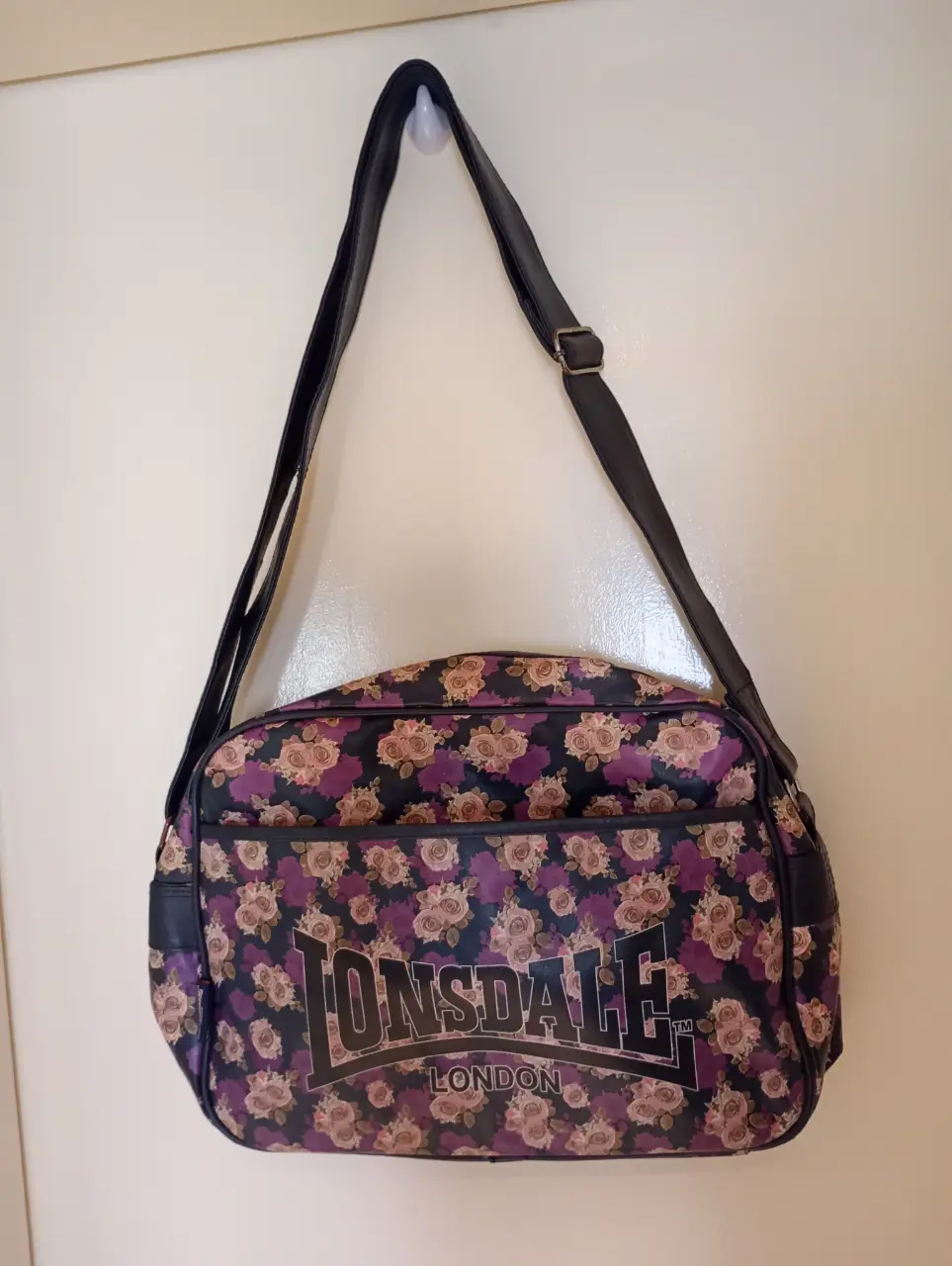 Bolso Lonsdale con estampado floral en tonos azules, rosas y violetas. Correa regulable. Posee un bolsillo delantero que se cierra con un abrojo. Ideal para la facu o lo que quieras! Entran aprox 4 cuadernos A4. Medidas: 40 cm ancho x 30 cm alto (aprox.). Muy poco uso!