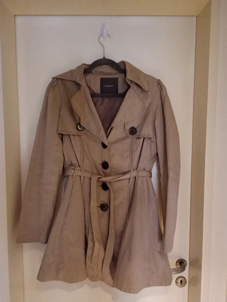 Trench coat beige de la marca Basement, con cinturón para ajustar la cintura y botones. Ideal para un look elegante y versátil.