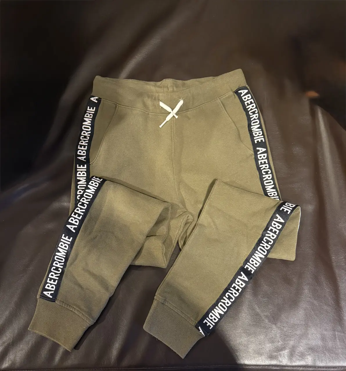Pantalón de jogging verde militar de Abercrombie Kids, con detalles de cinta lateral con el logo de la marca. Talle 13/14, ideal para un look casual y cómodo. Es para niño / adolescente muy poco uso 