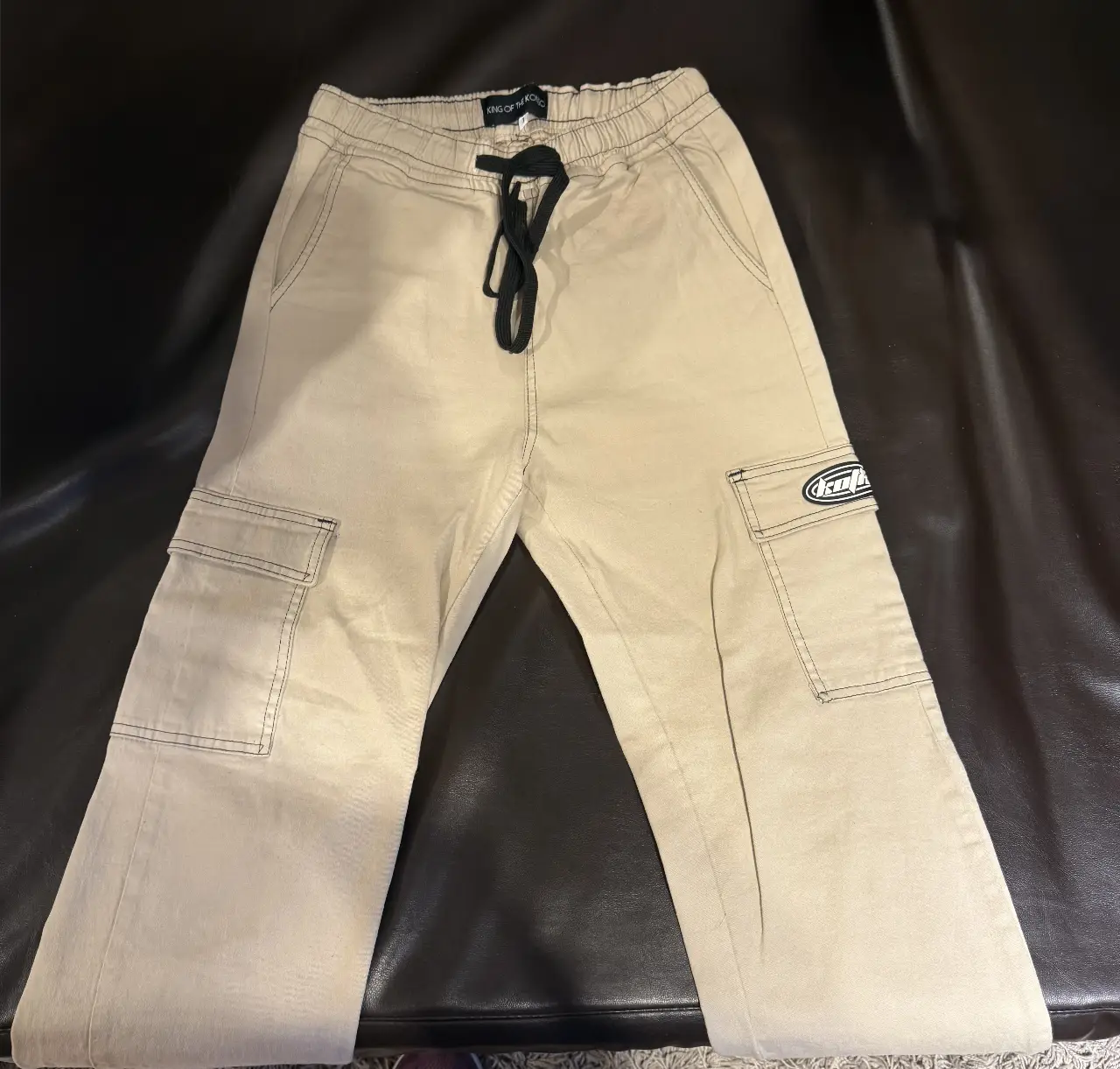 Pantalón cargo color crudo para adolescente  con bolsillos laterales y detalle de etiqueta de la marca. Talle 1, con cintura elastizada y cordón. 