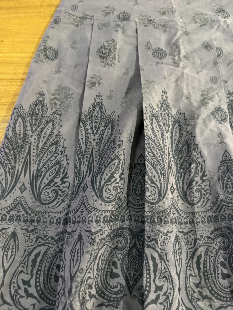 Pollera gris con estampado de flores y diseño paisley en tonos oscuros. Posee pliegues en la parte delantera.