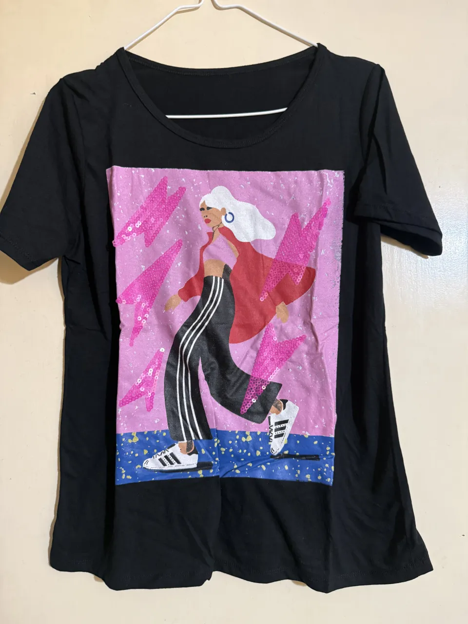 Remera negra con estampa de una mujer caminando. La estampa tiene lentejuelas rosas.