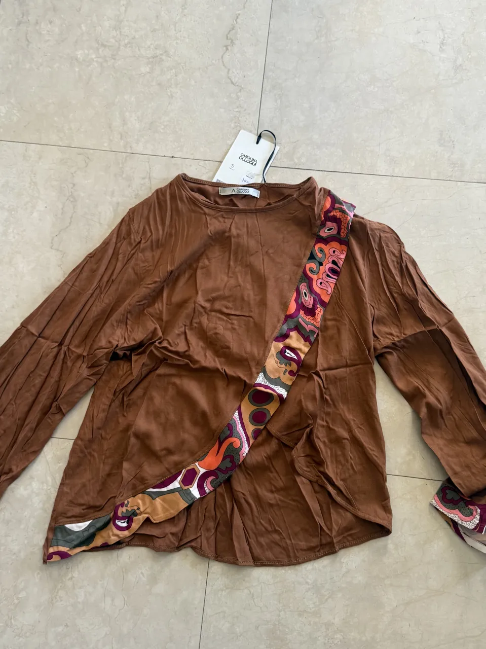 Remera marrón de manga larga con estampa psicodélica en diagonal sobre el frente y en el borde inferior de la manga derecha. Posee cuello redondo.