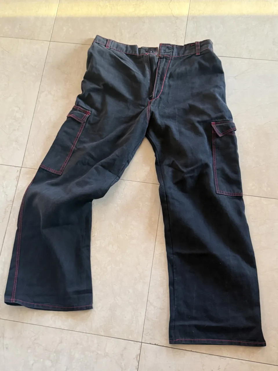 Pantalón cargo de gabardina color gris oscuro con costuras a la vista en color rosa. Posee bolsillos cargo en los laterales.