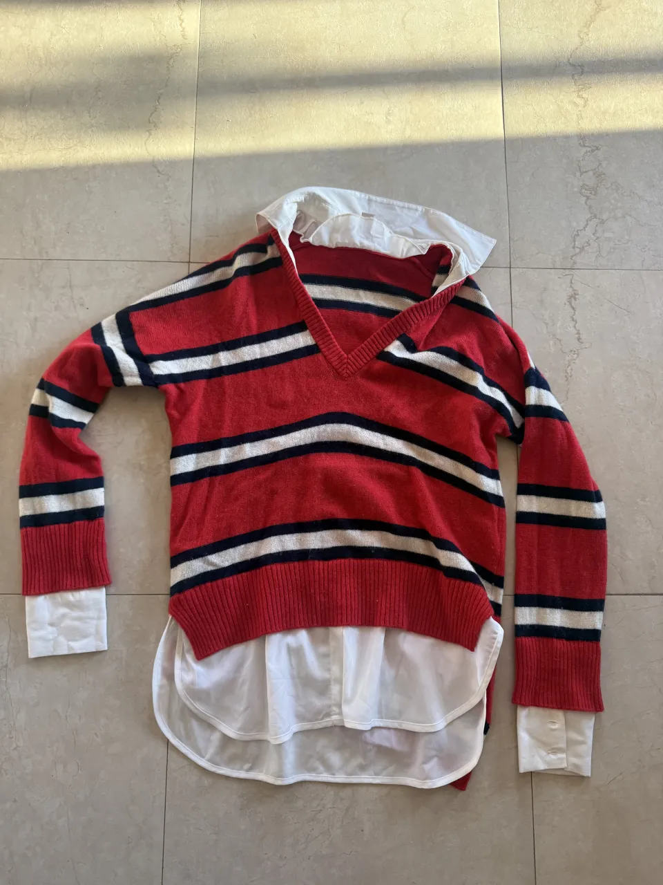 Remera de algodón a rayas rojas, blancas y negras con cuello de camisa blanco. Mangas largas y puños con botones.