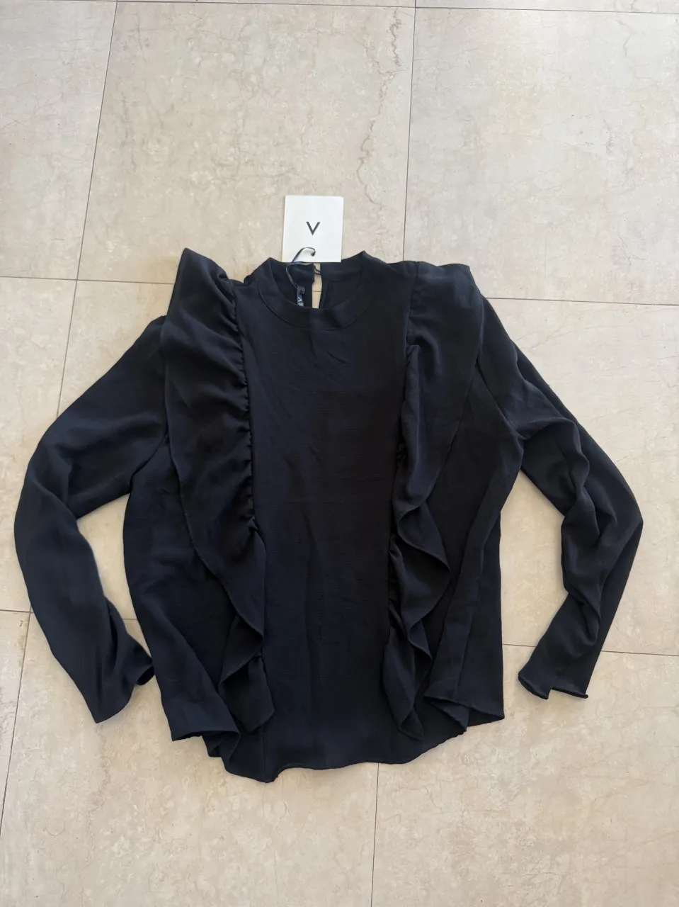 Blusa negra de manga larga con volados en el frente. Cuello redondo y cierre en la espalda.