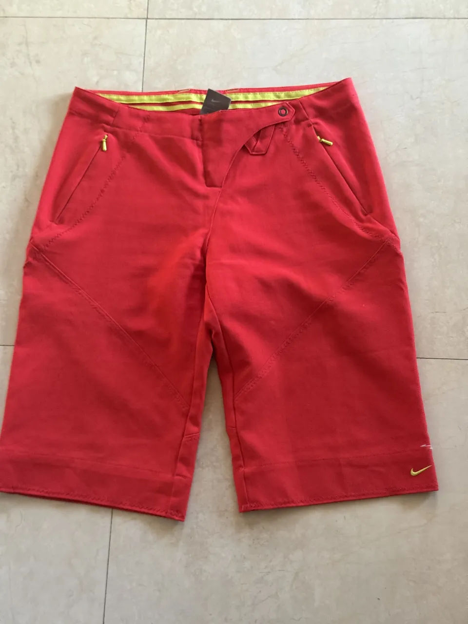 Shorts deportivos rojos con detalles en amarillo en la cintura. Tienen bolsillos laterales con cierre.