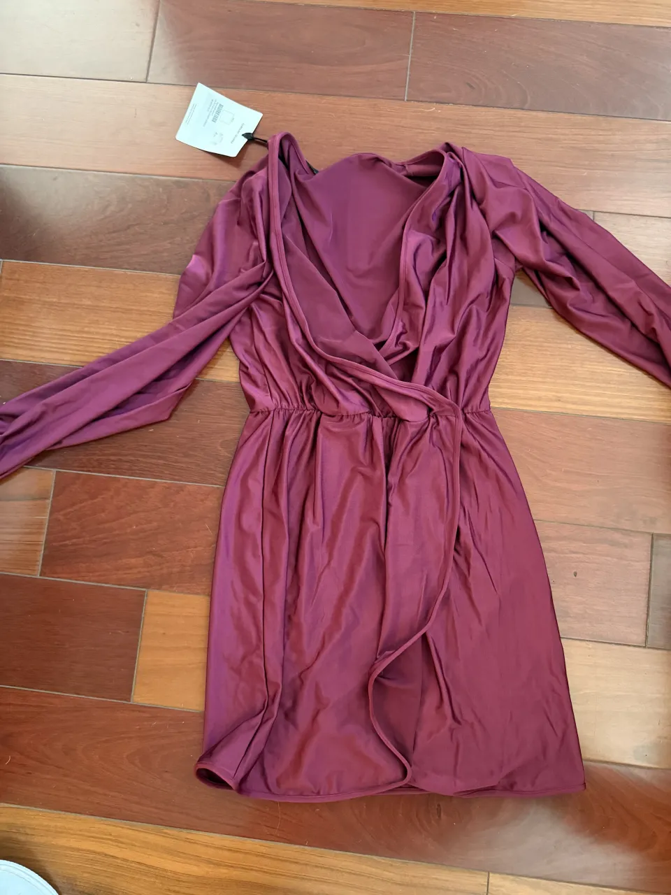 Vestido de manga larga con escote cruzado y cintura elastizada. La falda tiene un corte asimétrico con una abertura lateral.