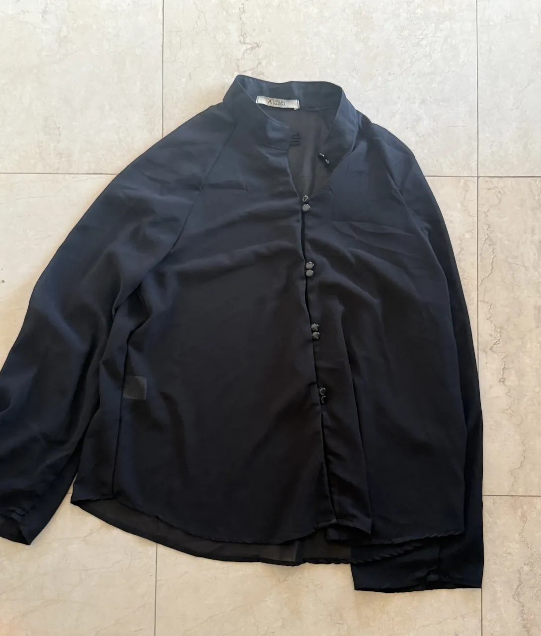 Camisa negra de manga larga con cuello mao y botones al frente.