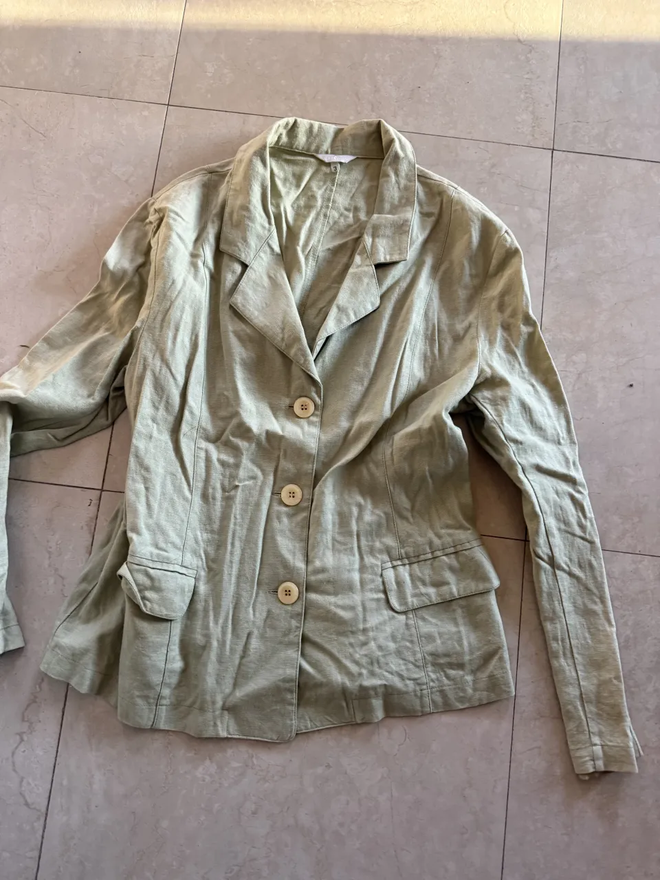 Blazer de lino color verde claro. Tiene dos botones al frente, dos bolsillos con solapa y mangas largas.