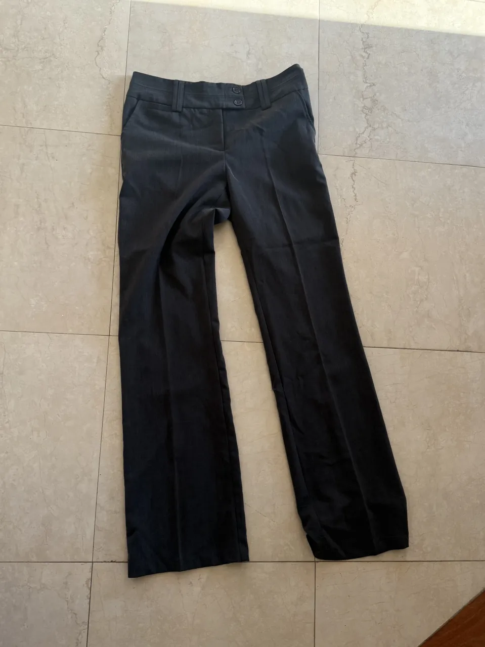 Pantalón de vestir gris oscuro con dos botones en la cintura y bolsillos delanteros.