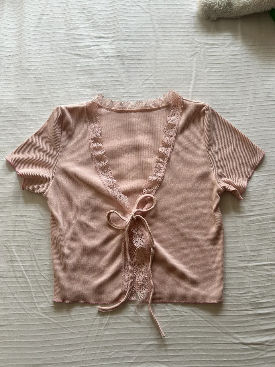Top rosa de manga corta con detalles de encaje en el escote y cierre de lazo al frente. Posee cuello redondo con terminación de encaje.