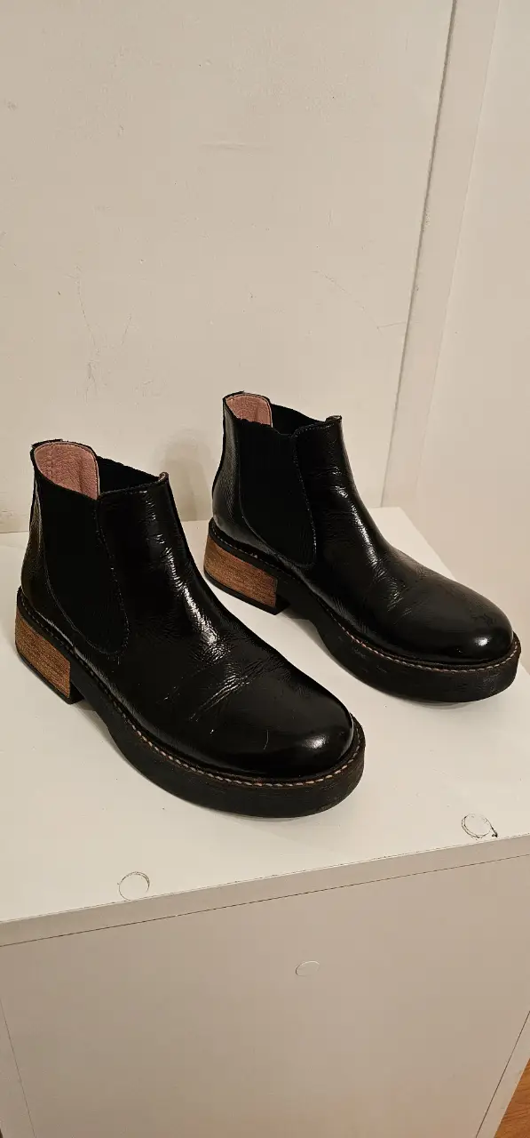 Botines negros de charol con taco de madera. Ideales para un look moderno y elegante.