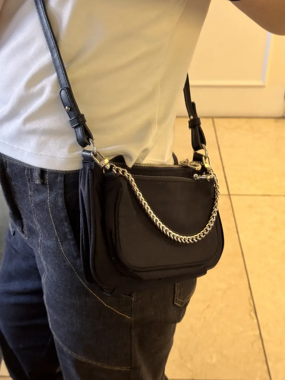 Bandolera negra con cadena plateada. Puede separarse. Tiene desgastes en una parte del cierre. se puede separar. 