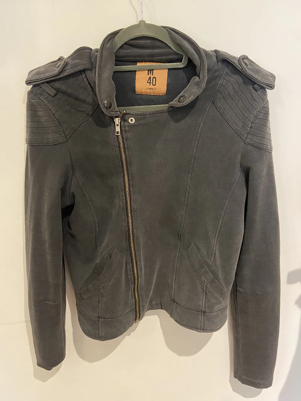 Campera estilo biker de tela gris oscura, con detalles en los hombros y cierre asimétrico. Talle M de la marca Complot.