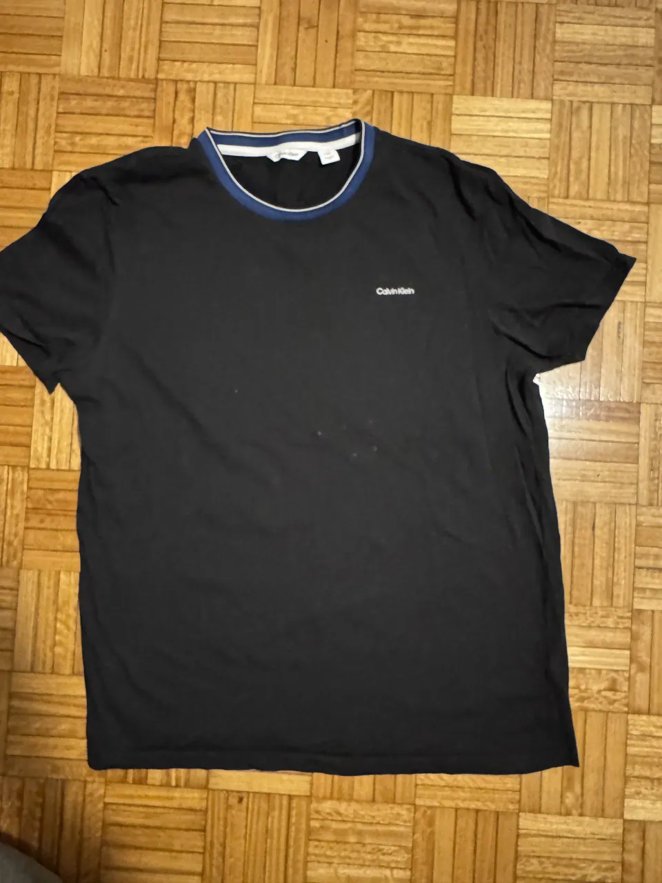 Remera negra de manga corta con cuello redondo y detalles en azul y blanco. Logo de la marca bordado en el frente. Ideal para un look casual y moderno.