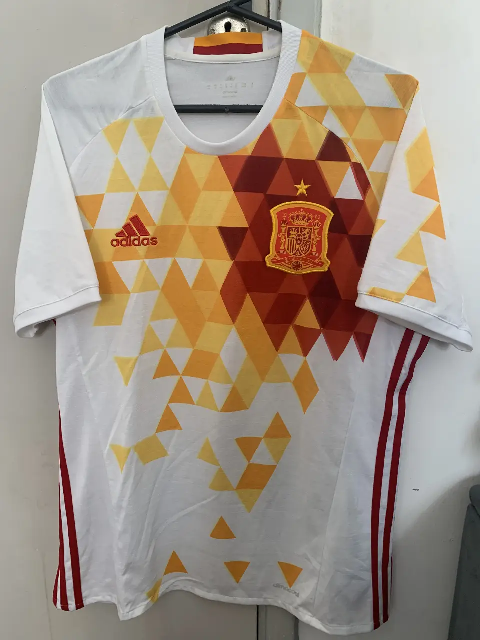 Camiseta de fútbol de la selección española, con diseño geométrico en tonos amarillos y rojos. Con el logo de Adidas y el escudo de España.