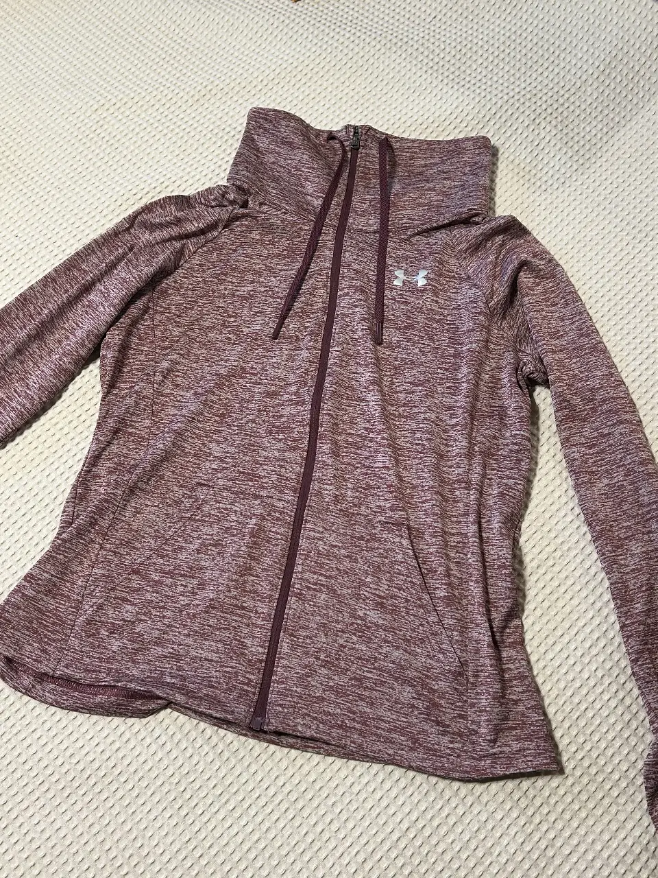 Buzo deportivo de mujer Under Armour con cierre completo y cuello alto. Tono borgoña jaspeado, ideal para actividades al aire libre o para un look casual y cómodo.