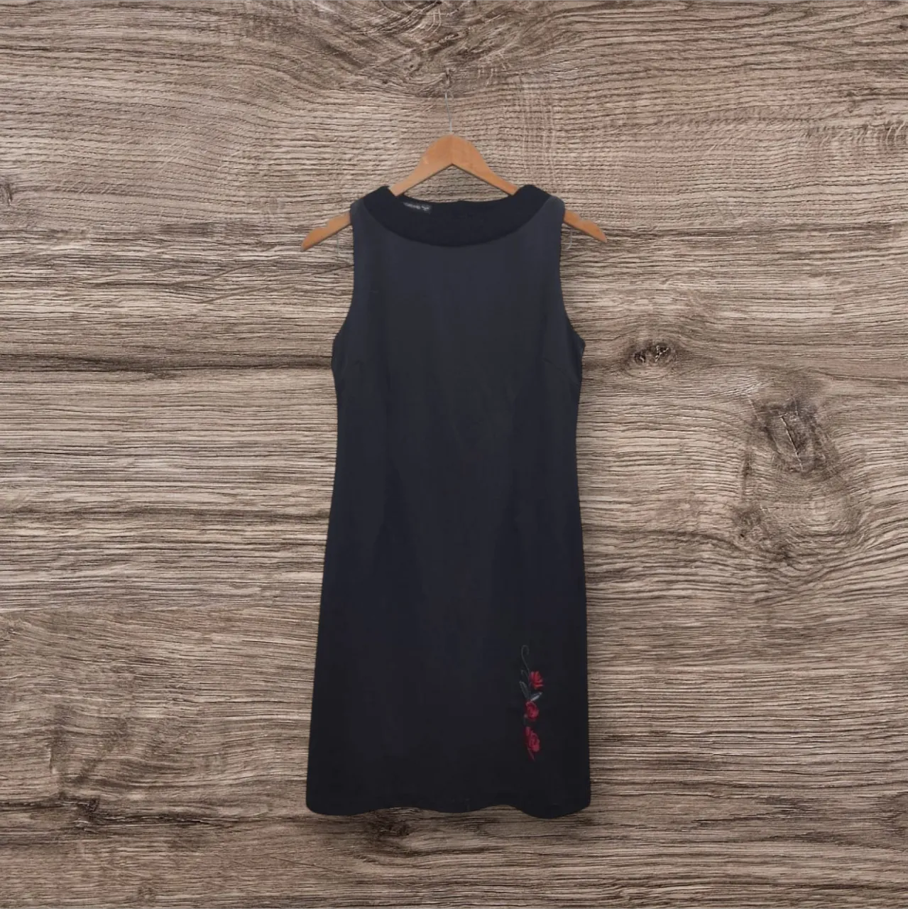 Vestido midi negro sin mangas con detalle de flores rojas en la parte inferior. Cuello redondo y cierre en la espalda. Ideal para una salida o evento semi-formal.