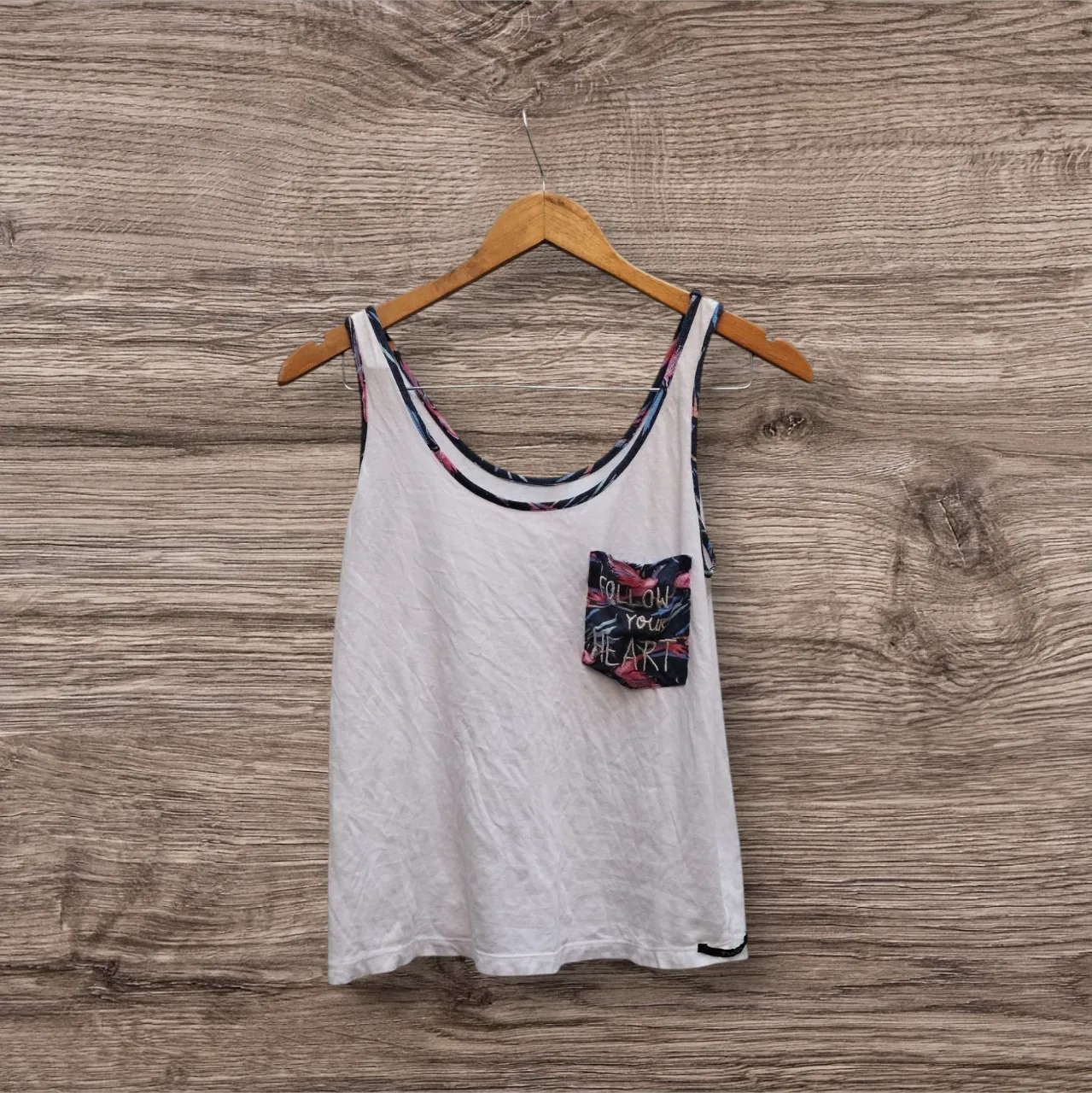 Musculosa blanca de mujer con bolsillo estampado floral y detalle en el cuello. Ideal para un look casual y fresco.