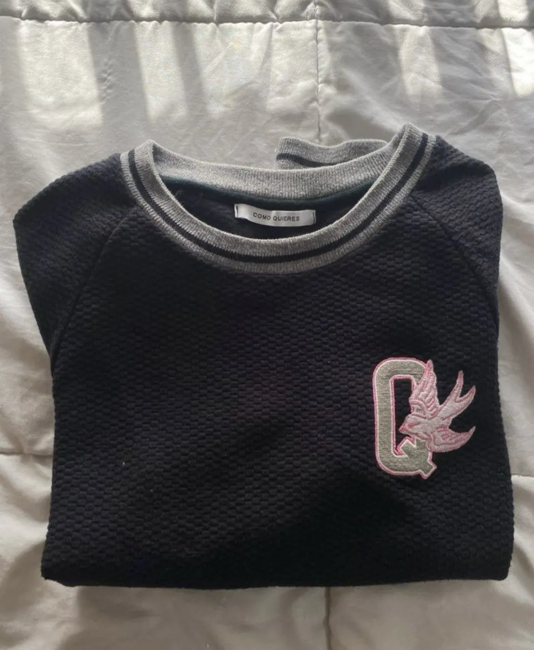 Buzo de cuello redondo negro con detalles grises y parche bordado. Ideal para un look casual y cómodo.